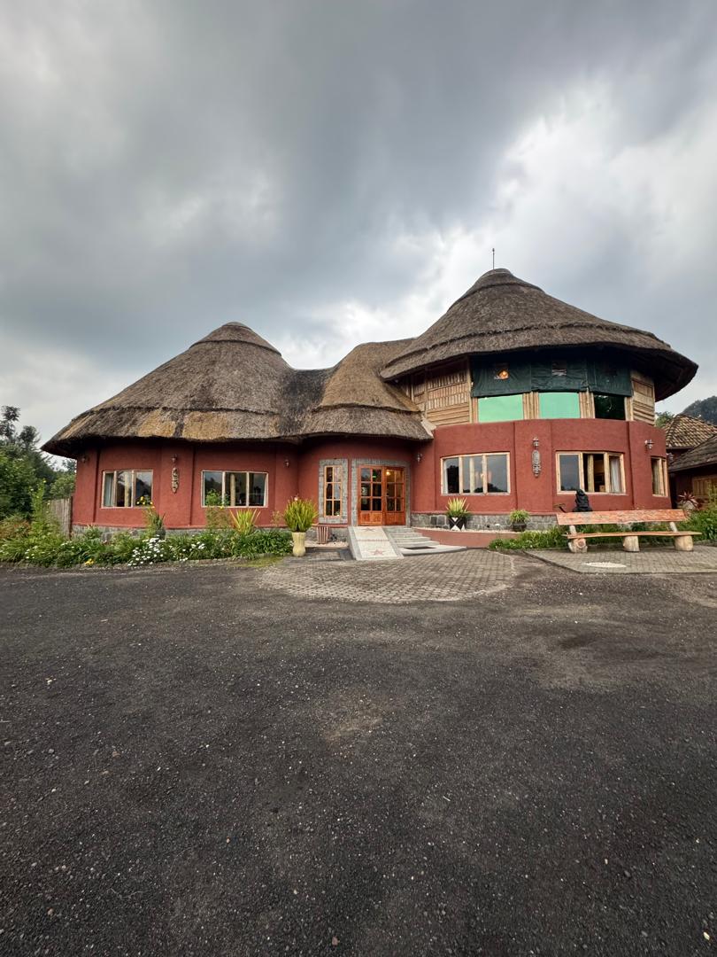 A large eco-lodge with round, thatched roofs and red walls sits in a rural setting near Volcanoes National Park